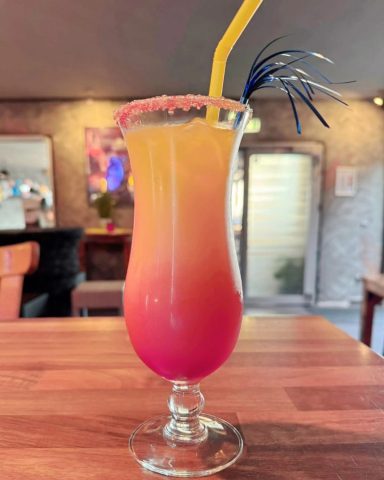 Cocktail in einem hohen Glas mit orange-rotem Farbverlauf und einem bunten Strohhalm.